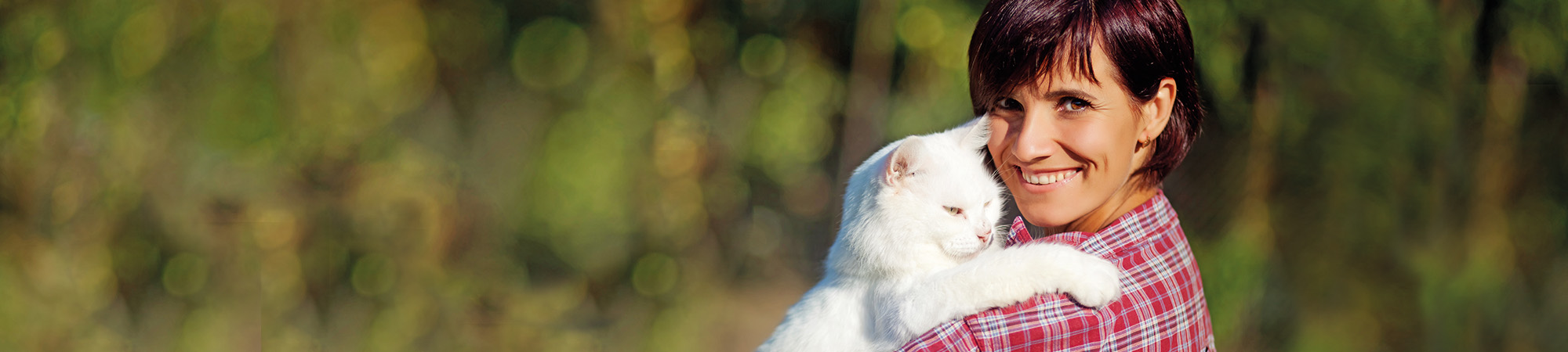 Frau schmust mit ihrer weißen Katze auf dem Arm in der Natur