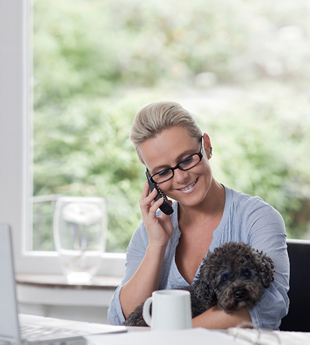 Frau mit Hund auf dem Schoß berät Kunden am Telefon und per Mail